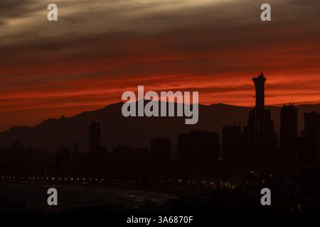 Photo of the sun setting in the evening over the old town of Benidorm in Spain showing the beautiful red sun set with clouds in the sky along side hig Stock Photo