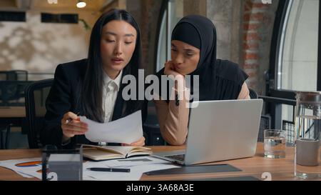 Female coworkers multiracial business women businesswomen Asian woman Arabian Muslim businesswoman in hijab discuss information data laptop document Stock Photo