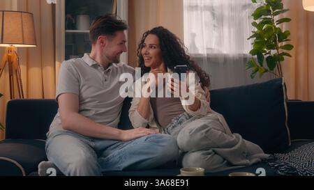 Multiracial positive happy couple family Caucasian man guy male Hispanic Latino woman girl female smile laughing talking using mobile phone together Stock Photo
