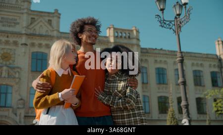 Two girls females women walking outside college academy high school university talking African man guy male run frighten surprise hugging happy Stock Photo