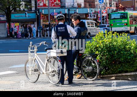 Japanese police officer issuing a fine to a cyclist wearing headphones on a street in Asakusa, Tokyo. Stock Photo