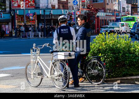 Japanese police officer issuing a fine to a cyclist wearing headphones on a street in Asakusa, Tokyo. Stock Photo