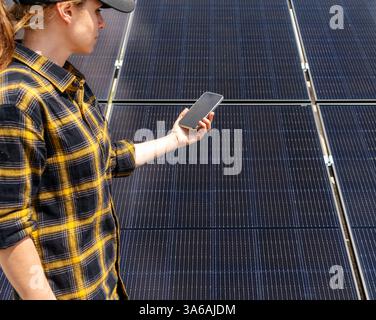 Female monitoring solar energy system using her mobile phone. Stock Photo