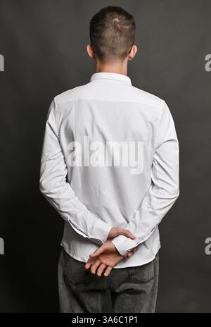 A vertical photo man's hands clasped behind his back, with one hand wrapped around the wrist of the other. The image conveys a sense of tension, patie Stock Photo