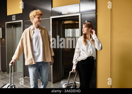 Loving couple stands in a stylish hotel hallway, sharing smiles while waiting for the elevator. Stock Photo