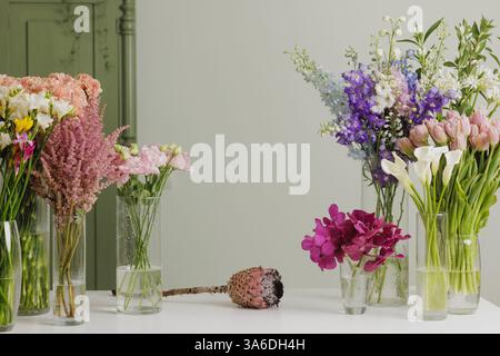 Elegant floral arrangement with fresh colorful flowers in glass vases on a white table against a soft green background, creating a serene atmosphere, Stock Photo