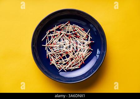 Collection of red-tipped wooden matches in dark blue bowl over bright yellow background Stock Photo