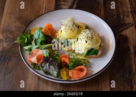 Breakfast plate with eggs benedict, smoked salmon and fresh greens salad on rustic wooden table Stock Photo