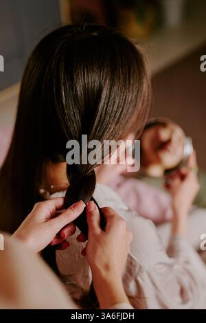 Vertical high angle shot of unrecognizable manicured hands braiding hair of woman Stock Photo