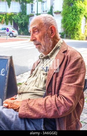 Older man sat at cafe table looking sad or fed-up - Preuilly-sur-Claise, Indre-et-Loire (37), France. Stock Photo