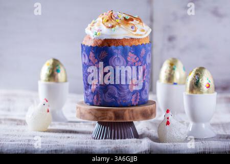 Easter cake, chocolate eggs in gold foil and chicken-shaped candles on a light background. Traditional Easter cake with meringue and colored sugar dec Stock Photo