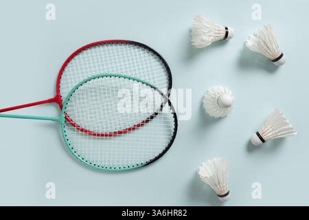White feather badminton shuttlecocks and two badminton rackets on light blue background. View from above. Concept racket sport. Leisure games. Stock Photo