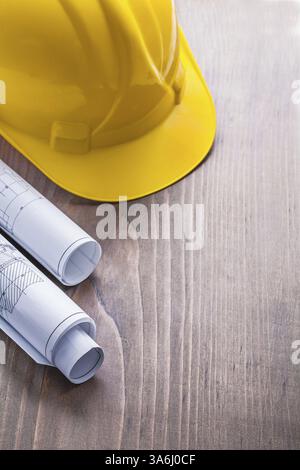 Rolled blueprints and yellow helmet on vintage wooden board with copyspace construction concept Stock Photo