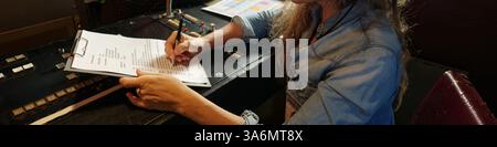 Header of modern female journalist sitting by workplace in TV van and taking notes in paper document during work Stock Photo