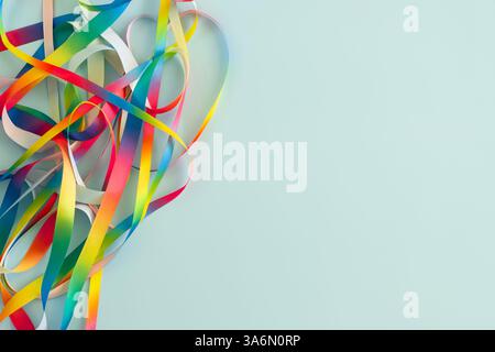 Abstract frame with multiple rainbow satin ribbons scattered in irregular pattern, gently twisted, curling and looping on light blue background. Top Stock Photo