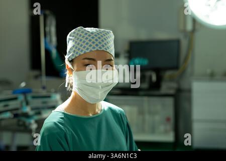 Asian female surgeon wearing mask and cap smiling confidently in operating room Stock Photo