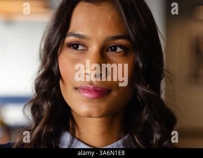 Confident woman with wavy hair looking away, thinking in modern office Stock Photo
