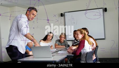 Teacher explaining math concepts to attentive students in classroom, using laptop. Education, teaching, technology, learning, engagement, instructing Stock Photo