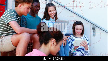 Students studying math together on school steps, using tablet and notebook. Education, teamwork, collaboration, technology, learning, outdoors Stock Photo