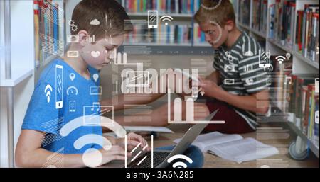 Image of digital interface with graphs and icons moving over two schoolboys sitting on floor in library studying using tablet and laptop. Global digit Stock Photo