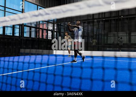 Playing padel tennis, two men focusing on hitting ball in indoor court Stock Photo