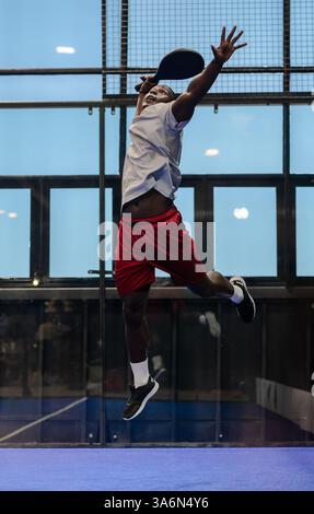 African American man jumping to hit ball during padel tennis match indoors Stock Photo