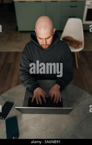 Vertical top view of serious male programmer in casual clothes typing code on laptop, developing software in dark home office, focused looking to Stock Photo