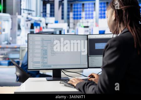 Photovoltaics factory programmer coding app monitoring system performance. Solar panels manufacturing plant system administrator writing code tracking energy production and efficiency Stock Photo