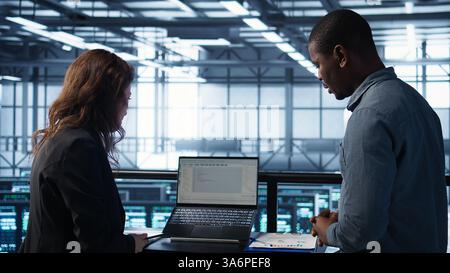 Teamworking data center computer scientists using artificial intelligence on laptop and tablet. Server room coworkers using neural networks AI on devices to do computing processes, camera B Stock Photo