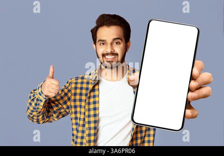 Positive Indian guy holding credit card and showing thumb up gesture on violet background Stock Photo