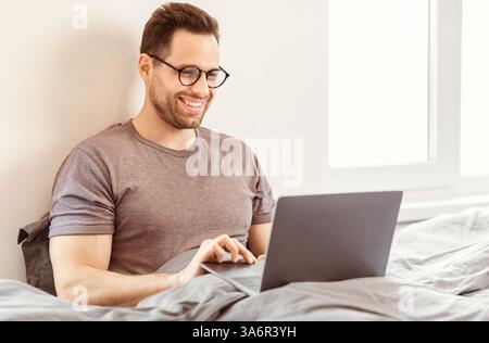 Man Using Laptop Browsing Internet Sitting In Bed At Home Stock Photo