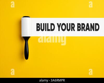 Branding, brand building and brand management concept. Lint roller with white trace on yellow colored background with the message build your brand. Stock Photo
