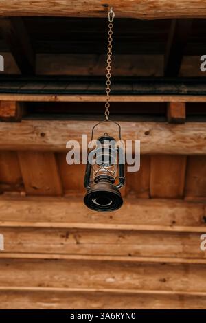 Traditional kerosene lamp hanging on wooden construction of a log cabin, vertical view Stock Photo