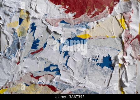 Dirty wall texture with peeled white, red, blue and yellow paper Stock Photo