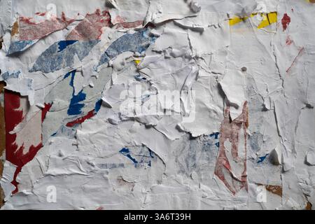 Dirty wall texture with peeled white, red, blue and yellow paper Stock Photo