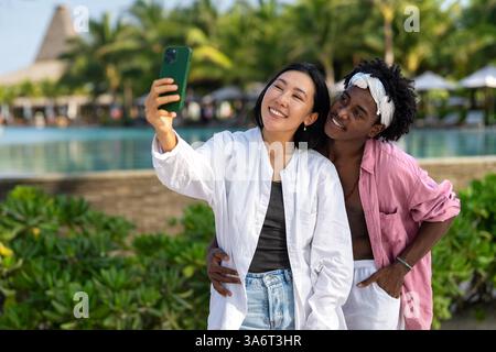 Trendy digital creator couple taking selfie by the beach, sharing travel content for social media Stock Photo