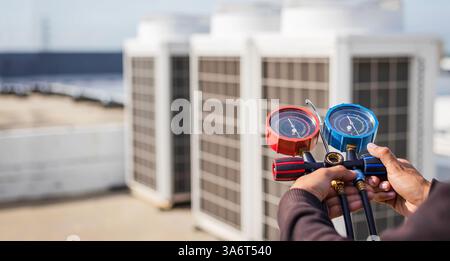 Air repair mechanic using measuring equipment for filling industrial factory air conditioners and checking maintenance outdoor air compressor unit. Stock Photo