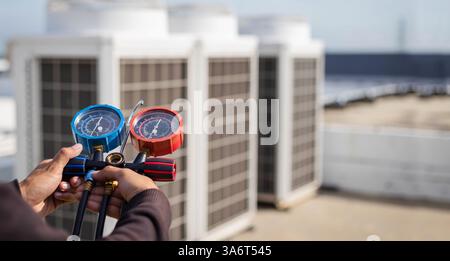 Air repair mechanic using measuring equipment for filling industrial factory air conditioners and checking maintenance outdoor air compressor unit. Stock Photo