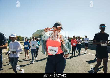 A multiracial group of runners participates in an outdoor race with a joyful and energetic atmosphere. The focus is on a smiling female athlete making Stock Photo