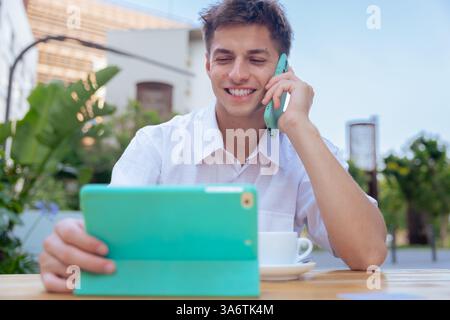Smiling caucasian businessman using tablet and phone at outdoor cafe table Stock Photo