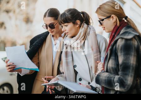 Three businesswomen collaborating outdoors while reviewing documents and discussing ideas Stock Photo