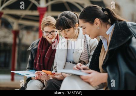 Three businesswomen collaborating outdoors on work materials and a mobile device Stock Photo