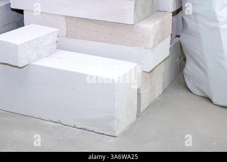 A neat pile of white bricks is positioned next to a large white bag, showcasing their contrasting textures and colors against each other Stock Photo