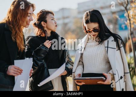 Three young women engaging in outdoor discussion with documents and a digital device Stock Photo