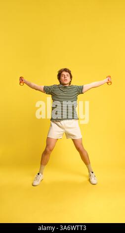 Dynamic photo of young man, focused on training jumping with spread wide hands with dumbbells against white background. Stock Photo