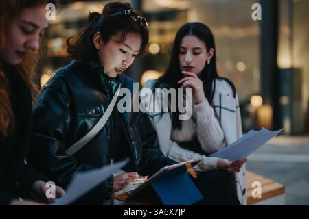 Young women collaborating outdoors, reviewing documents and using a digital tablet Stock Photo