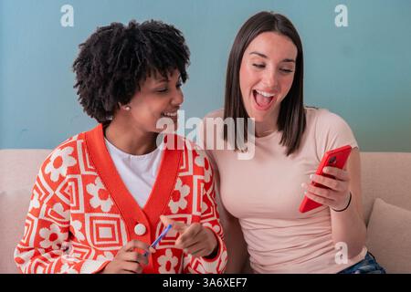 Two happy multiracial women shopping online with smartphone and credit card on the couch Stock Photo