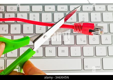 network cable is cut with scissors over a computer keyboard, symbolic photo sabotage Stock Photo