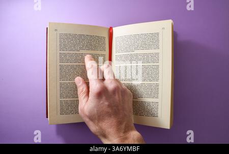 Concept of a person reading a book with a red registration tape pointing at text with your finger isolated on a purple background. Top view. Stock Photo