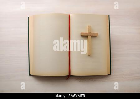 Open Bible with blank pages and wooden cross on top isolated on a wooden table. Top view. Stock Photo